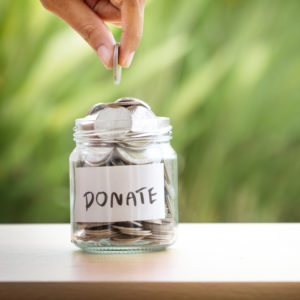 Hand putting Coins in glass jar for giving and donation concept